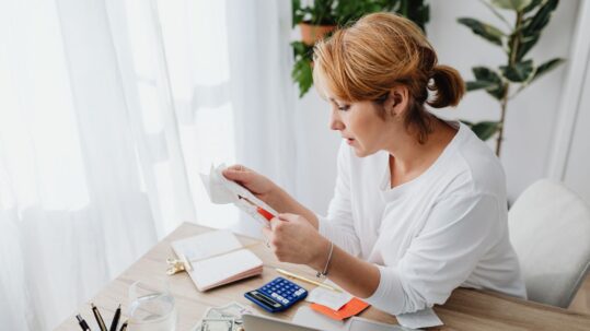 Small business owner at a desk reviewing receipts with a calculator and laptop