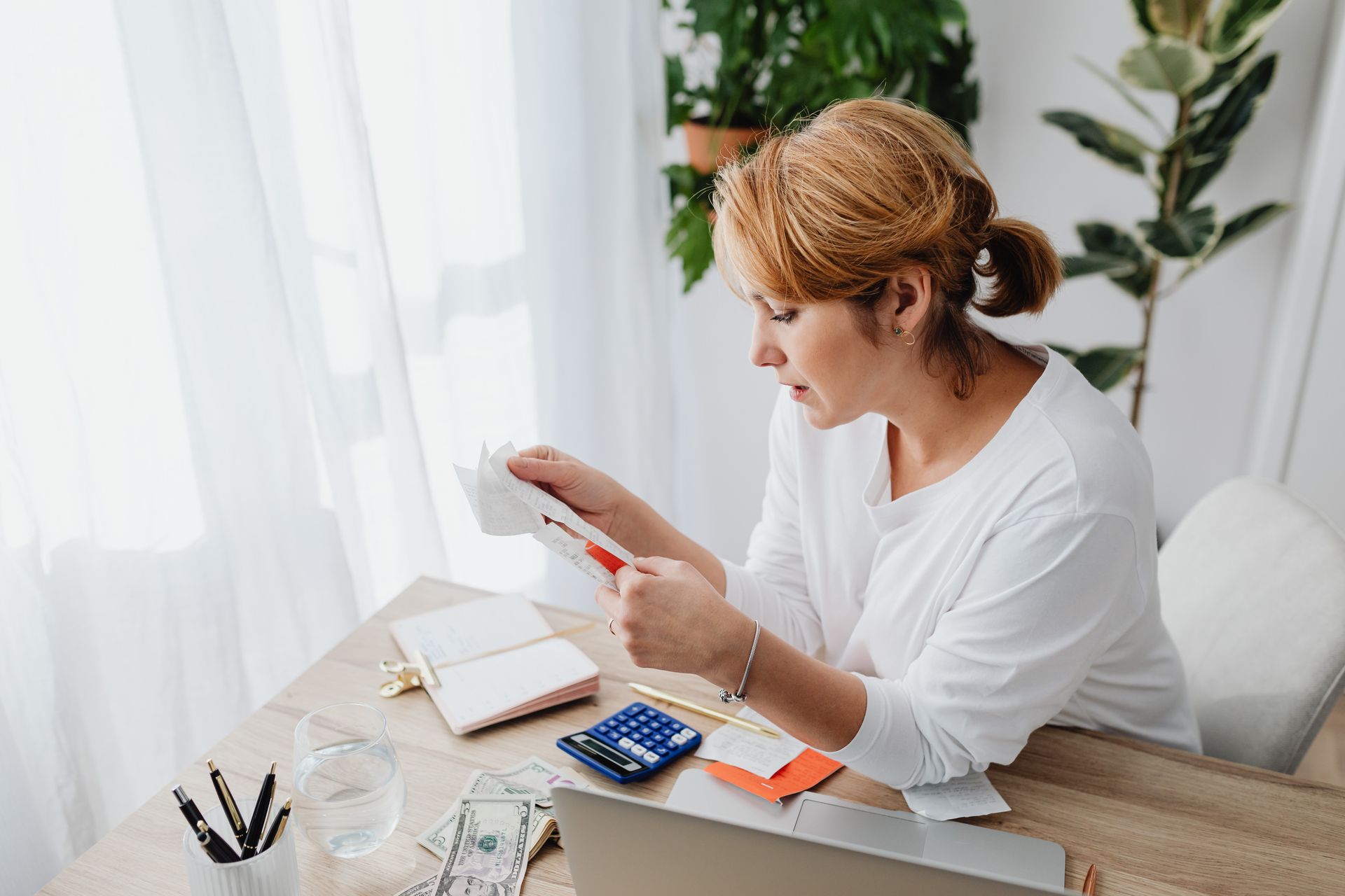 Small business owner at a desk reviewing receipts with a calculator and laptop