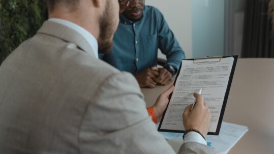 Hiring manager reviewing a contract on a clipboard with a candidate across the desk