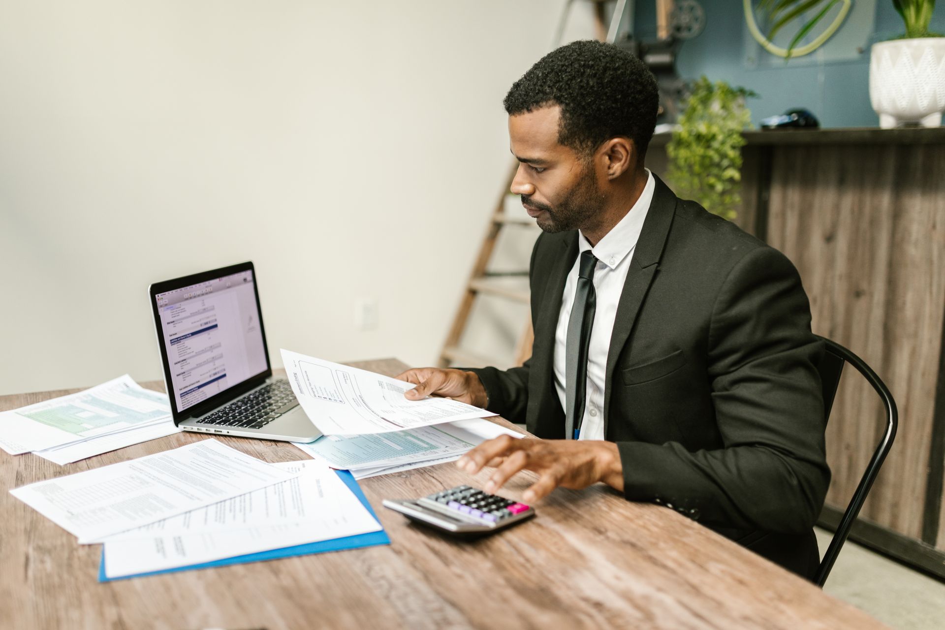 Finance professional in a suit reviewing financial documents with a laptop and calculator at a desk